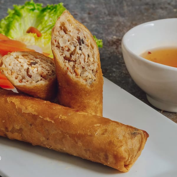Crispy Vietnamese egg rolls, one sliced open to show the savory filling, with lettuce and dipping sauce.