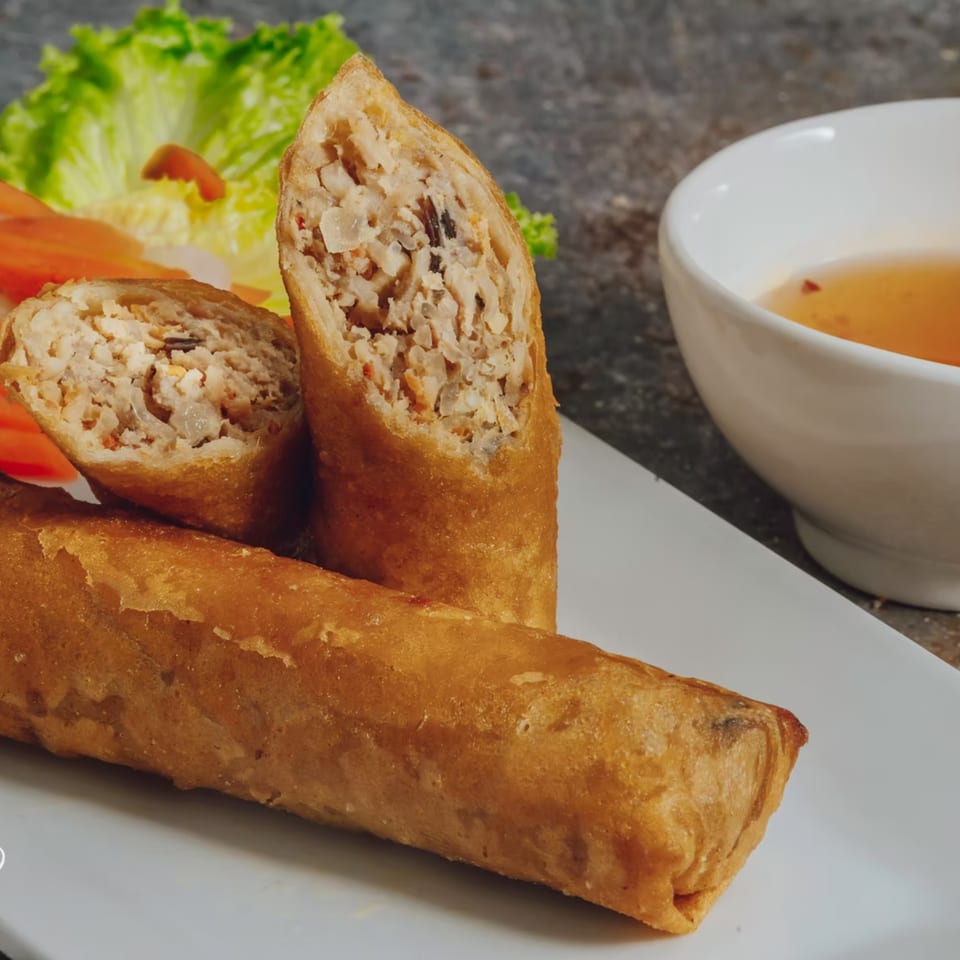 Crispy Vietnamese egg rolls, one sliced open to show the savory filling, with lettuce and dipping sauce.