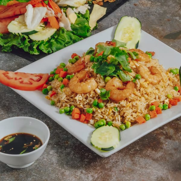 Shrimp fried rice with peas, carrots, and cilantro, served with a side of soy sauce.