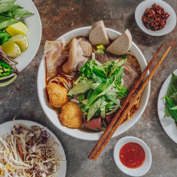 Overhead view of a Vietnamese pho bowl with various meats, herbs, and sides, chopsticks resting on top.